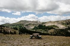 a picnic table in the middle of a field with mountains in the backgroud