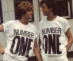 two young men standing next to each other in front of a building wearing numbers on their shirts