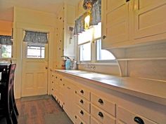 a kitchen with white cupboards and wooden flooring next to a dining room table