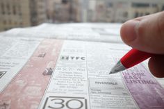 a person holding a red pen over a newspaper