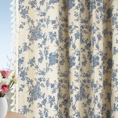 a vase with flowers on a table next to a curtain