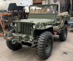 an army green jeep is parked in a garage next to some other vehicles and tools