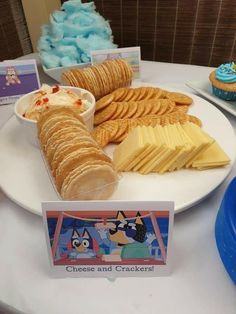 a plate with cheese and crackers on it next to cupcakes, cookies and other snacks