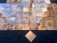 a tile floor with gold and blue tiles on it, including a square metal plate