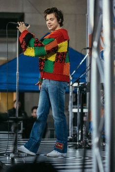 a man standing on top of a stage with a microphone in his hand and wearing a colorful sweater