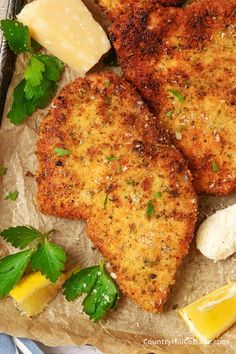 three pieces of fish with lemon wedges and parmesan cheese on the side