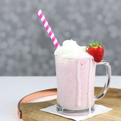 a strawberry milkshake with whipped cream and a pink striped straw is on a wooden tray