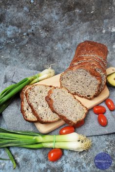 sliced loaf of bread sitting on top of a cutting board next to green onions and tomatoes