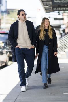 a man and woman are walking down the sidewalk together, both wearing black jackets and jeans