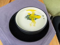 a white bowl filled with yellow liquid on top of a black plate