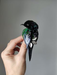 a hand holding a small black and green bird with leaves on it's tail