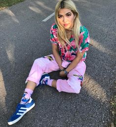 a woman sitting on the ground with her legs crossed wearing pink sweatpants and blue sneakers