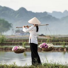 a woman carrying two baskets with flowers on her shoulders and one holding a stick over her head