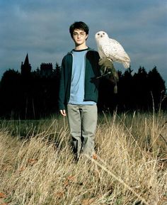 a young man holding an owl on his arm while standing in a field with tall grass