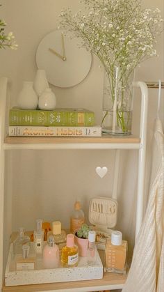 a shelf filled with cosmetics and flowers on top of a white dresser next to a clock