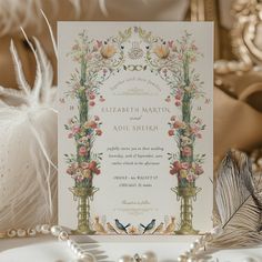 an ornate wedding card with flowers and feathers on the table next to pearls, beads and other accessories