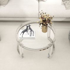 a glass coffee table with flowers in a vase on it and a white couch behind it