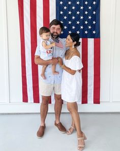 a man and woman holding a baby in front of an american flag