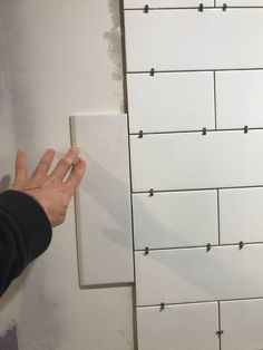 a person's hand is on the wall next to a white cabinet with square knobs