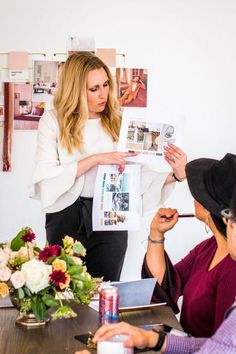 two women are sitting at a table and one woman is holding up a magazine while the other looks on