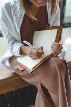 a woman sitting on a bench writing in a note book with a pen and paper