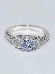 a white gold engagement ring with three stones on the side and an intricate band around it