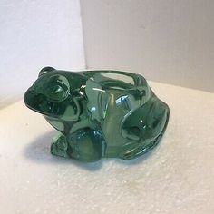 a green glass frog figurine sitting on top of a white countertop next to a wall