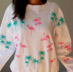 a woman wearing a white sweater with pink flamingos and palm trees on the front