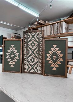 three framed art pieces sitting on top of a table next to each other in front of a bookshelf