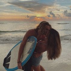 a man and woman kissing while holding a surfboard in front of the ocean at sunset