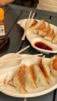 two plates filled with dumplings and chopsticks next to sauce on a table