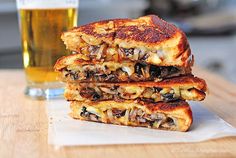 two grilled sandwiches stacked on top of each other next to a glass of beer