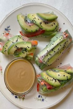 cucumber wrapped in leafy vegetables with dipping sauce on a white and floral plate