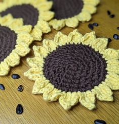 three crocheted sunflowers sitting on top of a wooden table next to seeds