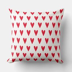 a red and white pillow with hearts printed on the front, sitting against a wall