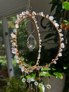 a gold and crystal sun catcher hanging from a tree in front of a window with potted plants