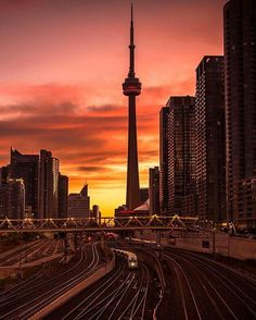 the sky is red and orange as the sun sets over train tracks in front of tall buildings