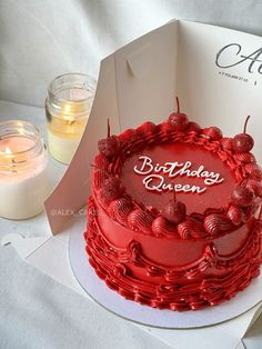 a red birthday cake sitting on top of a table next to a box and candle