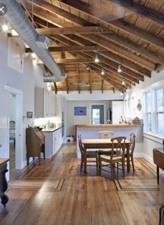 an open kitchen and dining room with wood flooring, exposed ceiling beams and white walls