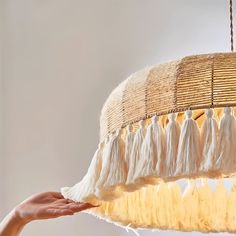 a person is holding up a light fixture with fringes on the bottom and sides