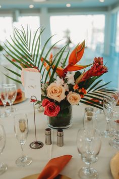 an arrangement of flowers and greenery in a vase on a table with wine glasses