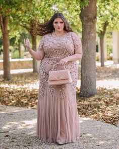 a woman in a long pink dress is holding her hand out while standing on the sidewalk