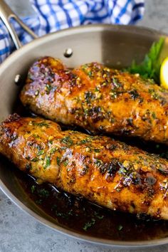 two cooked fish fillets in a pan with lemons and parsley on the side