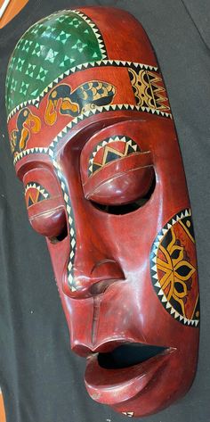 a red mask with green and yellow designs on it's face sitting on a black background