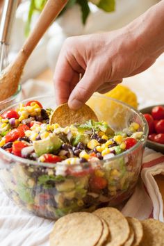 a person dipping a tortilla chip into a bowl filled with mexican salad ingredients