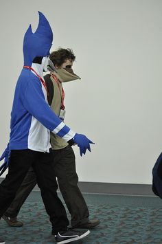 two people in blue costumes walking down a carpeted floor with one person wearing a mask