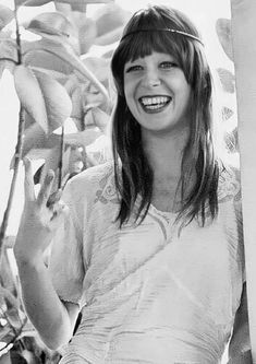 a black and white photo of a woman smiling with bananas on the tree behind her