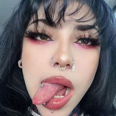 a woman with black hair and piercings sticking out her tongue