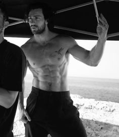 two shirtless men standing under an umbrella on the beach in black and white photo