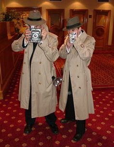 two men in trench coats taking pictures with their cell phones